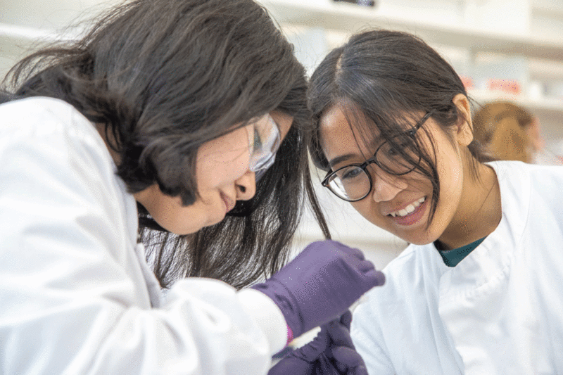 A teacher and a young woman are looking at a test tube in a lab